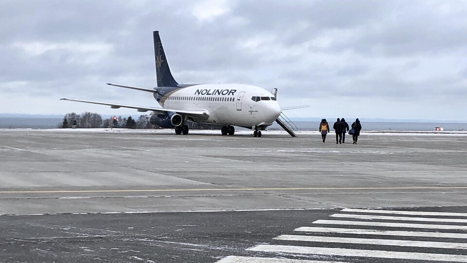 Quatre personnes se dirigent vers l'avion de Nolinor sur la piste de l'aéroport de Mont-Joli le 18 décembre 2019.