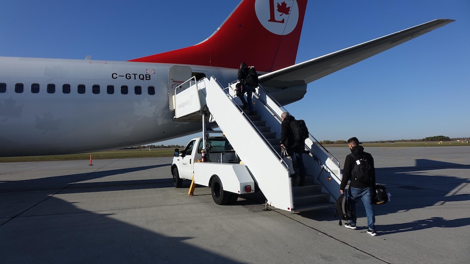 Des hommes chargés de sacs et de valises montent à bord d'un avion.