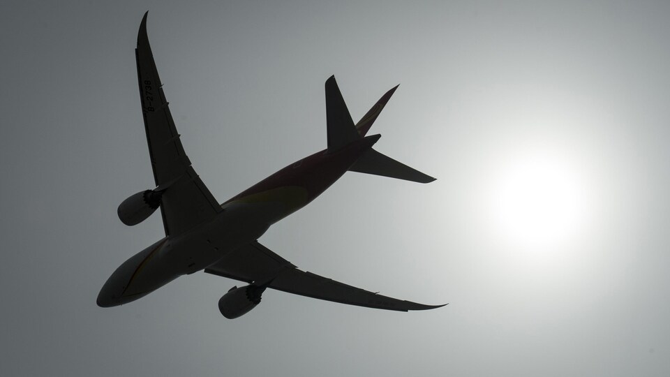 La silhouette d'un avion se détache dans un ciel couvert.