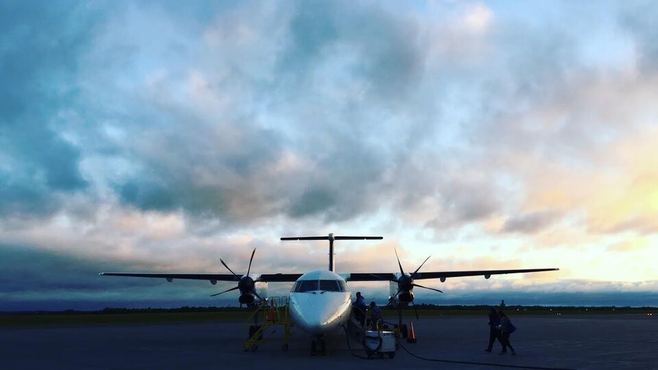 Un avion sur la piste, en arrière plan un coucher de soleil et un ciel nuageux.