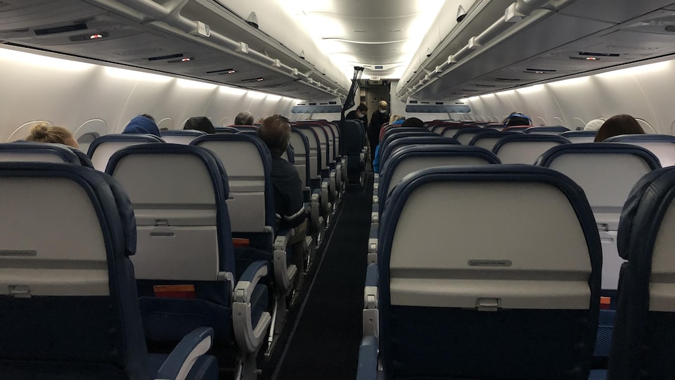 On voit de dos les sièges de l'avion qui sont peu occupés.
