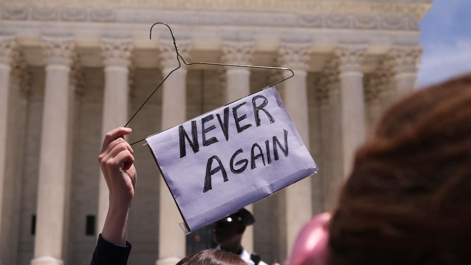Une femme tient un cintre sur lequel est écrit <br> «Plus jamais».