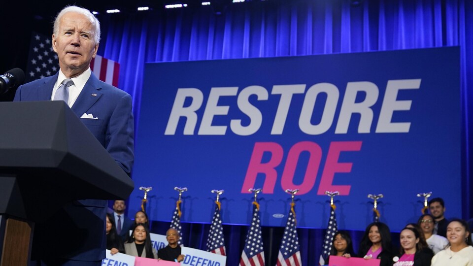 Joe Biden s'adresse à la foule devant une grande affiche où est inscrit Restore Roe. Plusieurs personnes tiennent des pancartes en faveur de du droit à l'avortement derrière lui. 