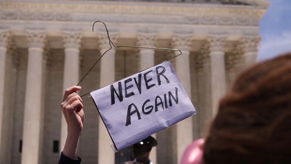 Une femme brandit un cintre de métal sur lequel est accrochée une pancarte sur laquelle il est écrit en anglais: «Plus jamais» en lettres majuscules.