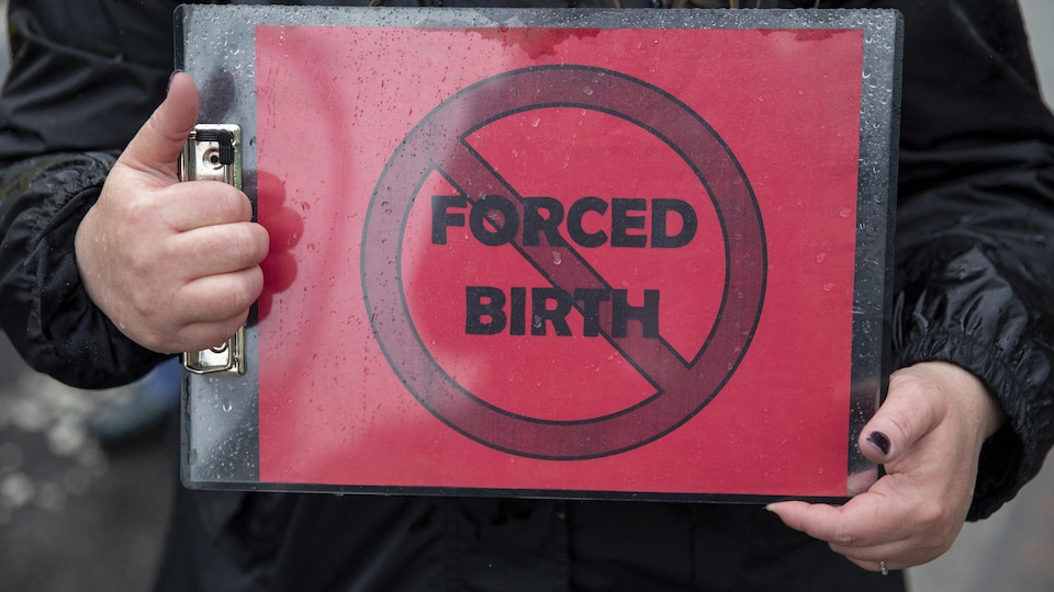 Une personne tient une feuille sur laquelle les mots suivants sont barrés : naissance forcée. Photo prise le 7 mai 2022 devant la Cour suprême des États-Unis.