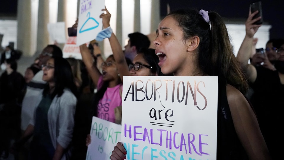Des personnes manifestent. Parmi elles, une femme tient une pancarte où il est écrit : « Les avortements sont des soins de santé nécessaires »