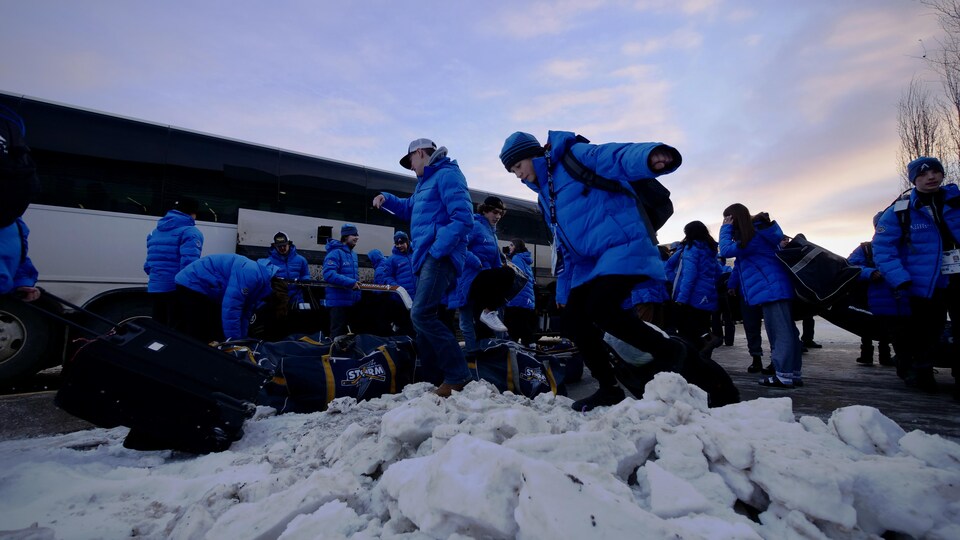 Des athlètes récupèrent leurs bagages dans la neige à côté d'un autocar.