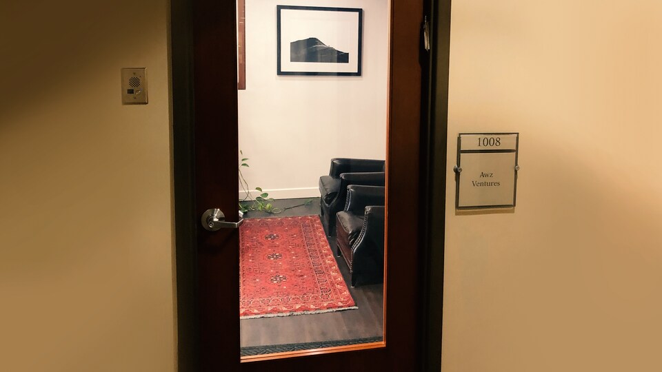 Derrière une porte vitrée, on peut voir deux fauteuils et un tapis. À côté de la porte, il est écrit : 1008, Awz Ventures