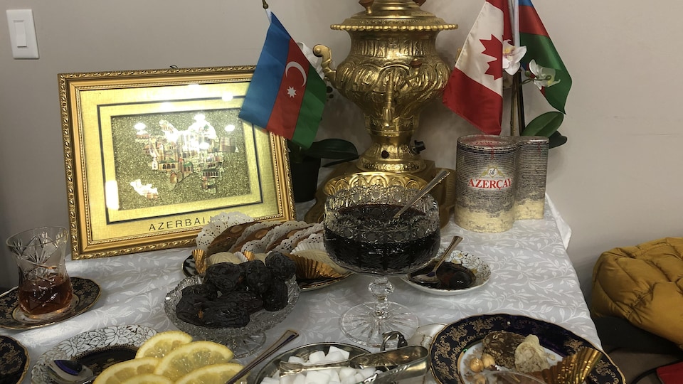 Une table sur laquelle sont placés notamment une tasse en verre, des gâteaux, des drapeaux canadien et azerbaïdjanais et une coupe en verre.