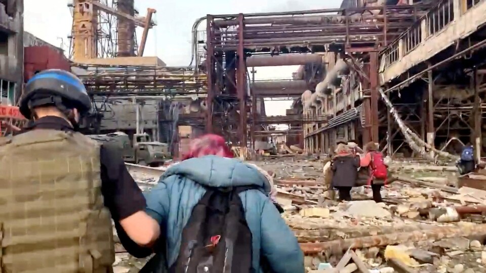 Fighters escort civilians to a devastated industrial scene. 