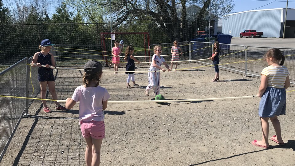 Des enfants sur un terrain tiennent des cordes et se passent un ballon.