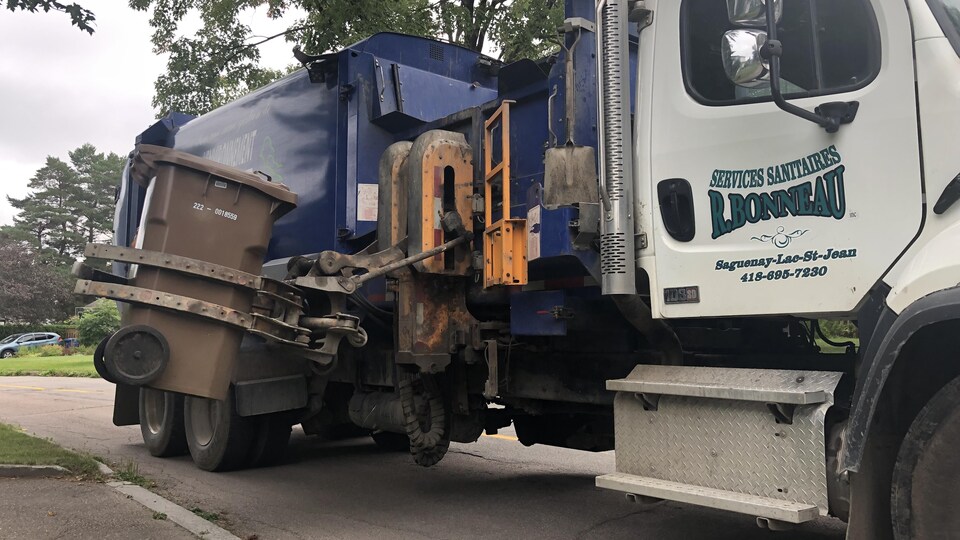 La pince d'un camion agrippe un bac brun.