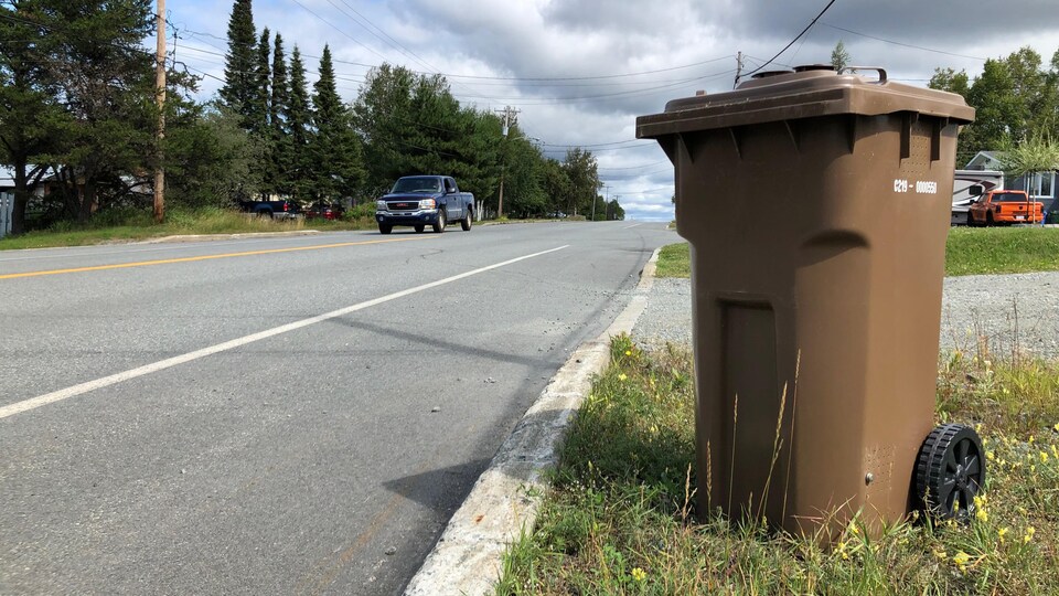 Un bac brun sur le bord d'une rue dans un quartier résidentiel.