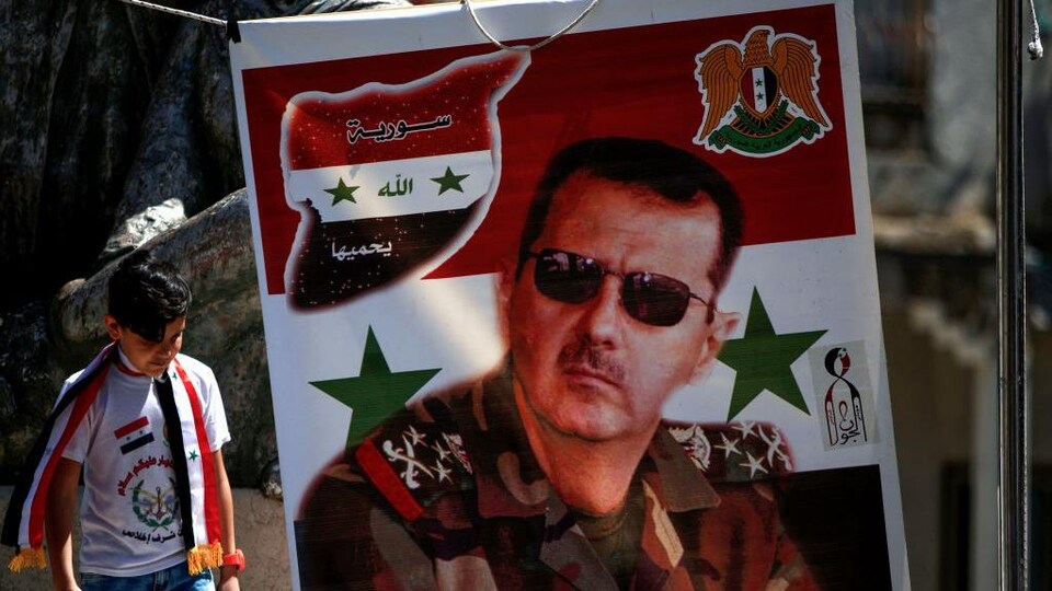 Un jeune garçon passe près d'une bannière sur laquelle figure le portrait de Bachar Al-Assad.
