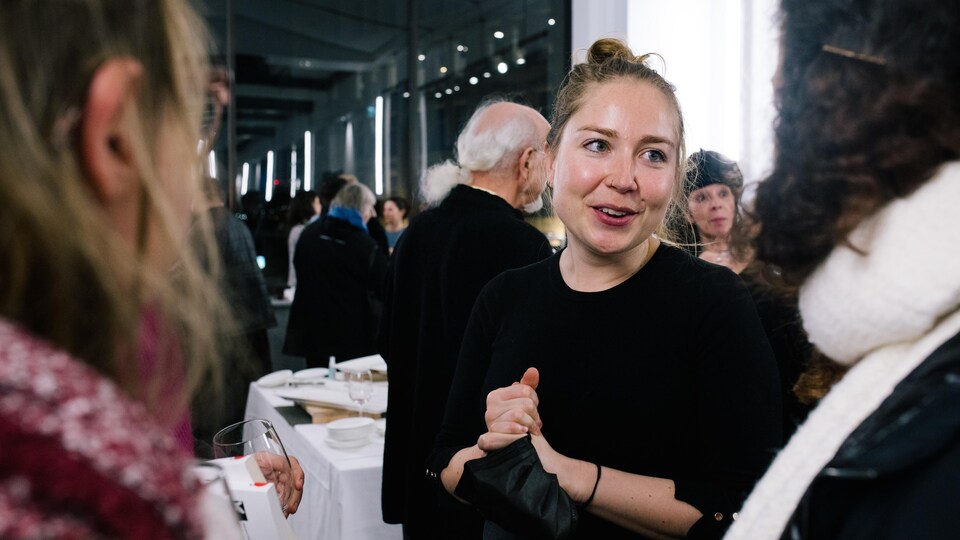 Une jeune femme parle à deux autres personnes lors d'une soirée publique.
