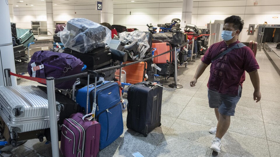 Un homme marche devant un amoncellement de valises empilées.