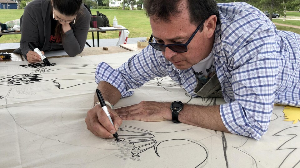 Un homme est penché sur une fresque et dessine avec un crayon.