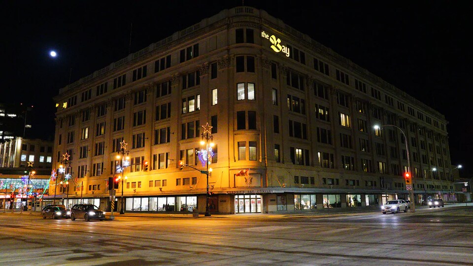 La façade du bâtiment de la Baie d'Hudson dans la pénombre avec des lumières de Noël tout près. 