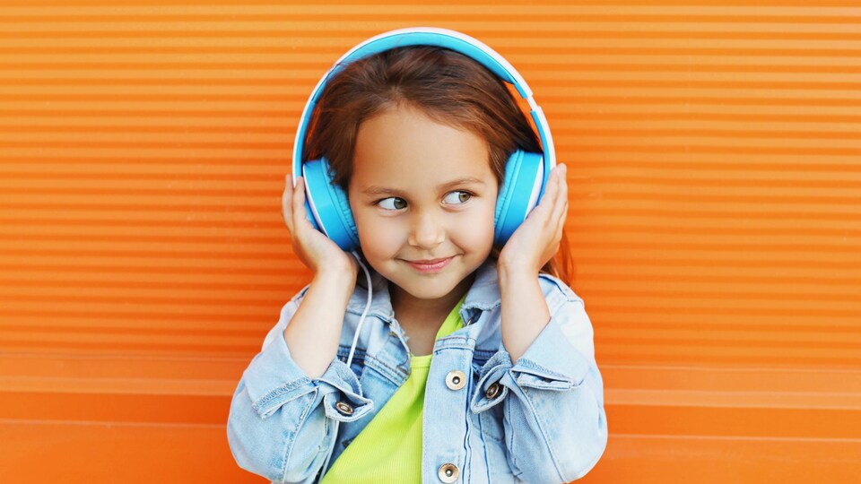 Une enfant écoute quelque chose qui la fait sourire avec des écouteurs bleus.