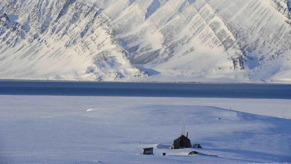 Une cabane en bois devant une montagne enneigée. 