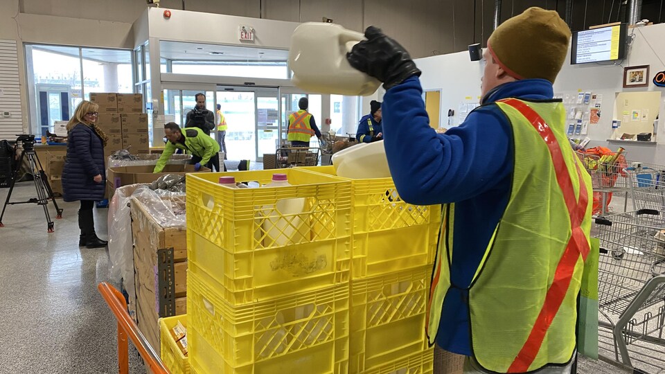 Dans un entrepôt, un homme remplit des caisses de bouteilles de lait. 