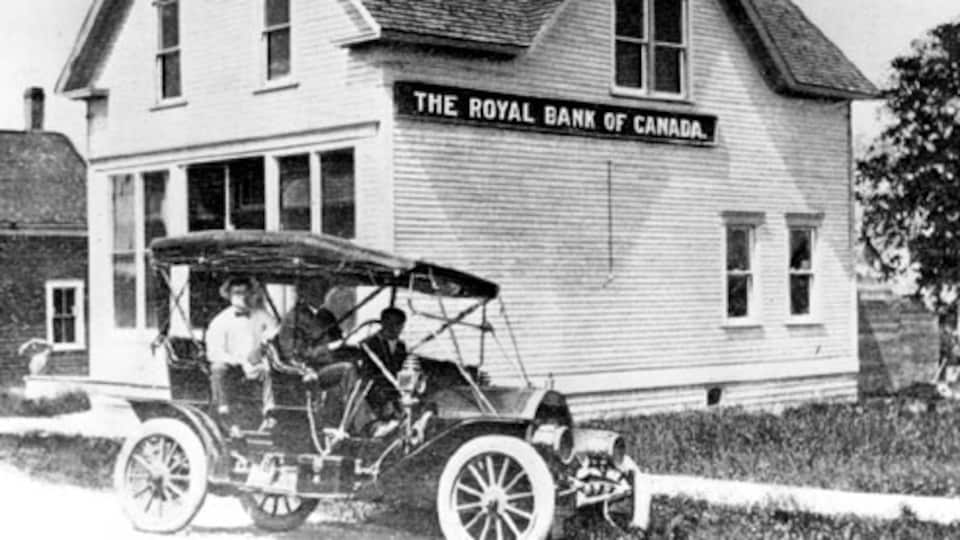 Une vieille voiture avec trois hommes à bord devant une banque 