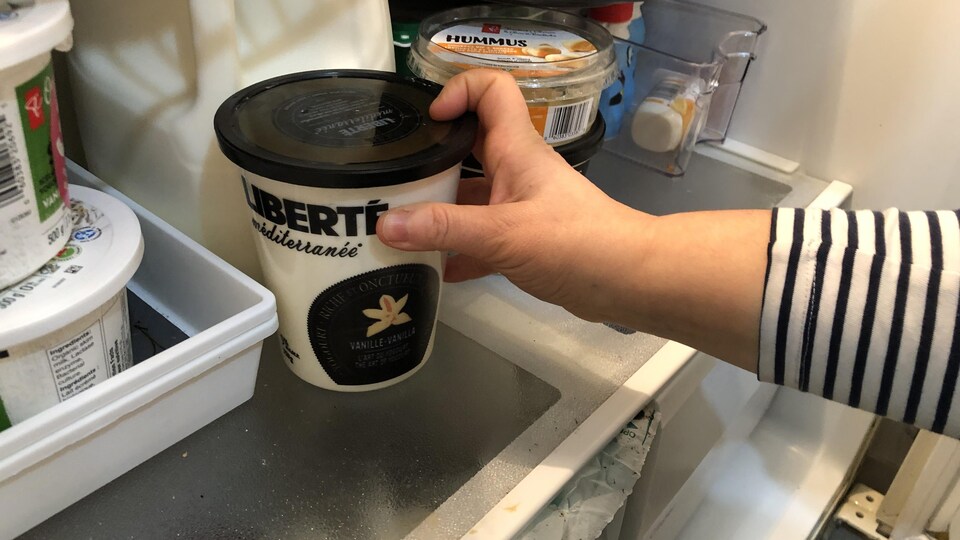 Une main dépose un pot de yogourt dans un réfrigérateur.