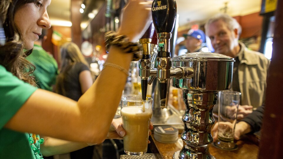 Une serveuse remplit un verre de bière dans un bar. Ni les clients ni elle-même ne portent un masque.