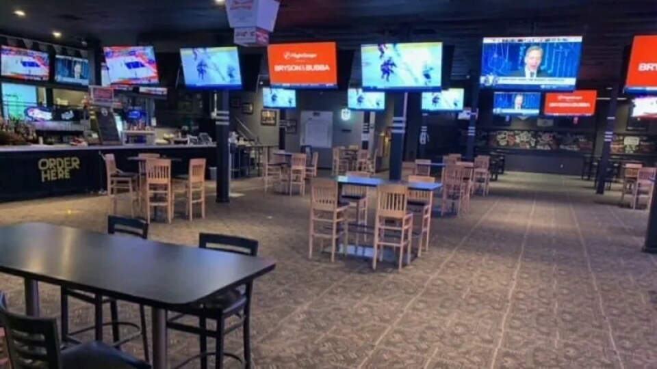 Photo de l'intérieur du bar Sports On Tap, à Saskatoon. On voit le bar à gauche, des tables avec la distance physique et de nombreuses télés accrochées un peu partout.