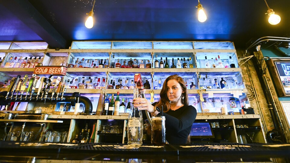 Une femme devant des étagères pleines de bouteilles d'alcool.