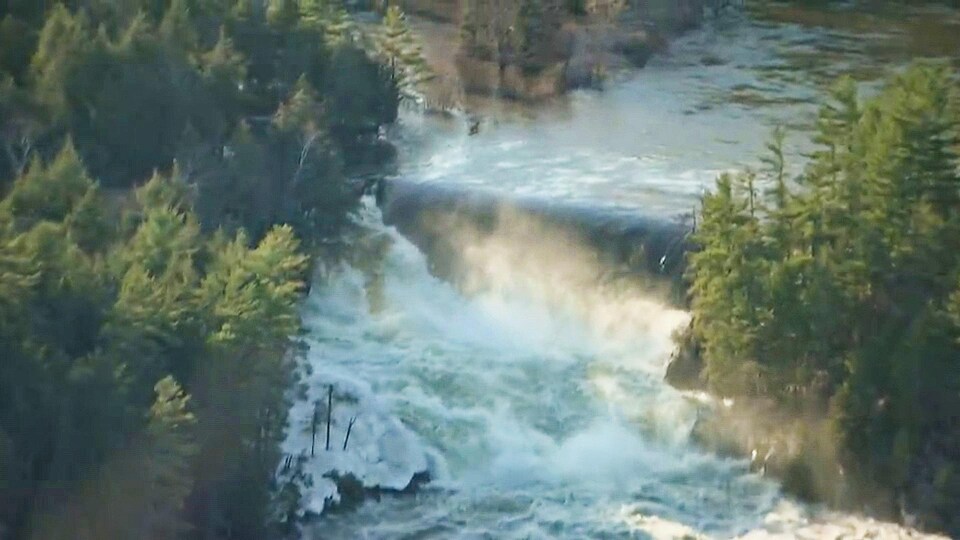 Un cours d'eau passe par dessus un barrage, entouré de forêt.