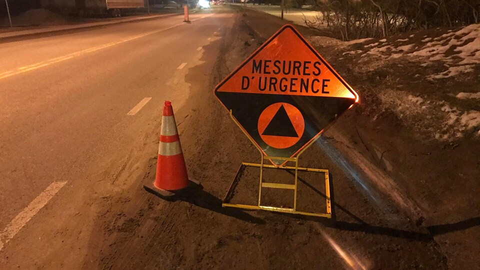 Un barrage routier de la Sûreté du Québec, qui vise à restreindre les visites non essentielles dans certaines régions du Québec, afin de limiter la propagation de la COVID-19 au sein de la population. On aperçoit une plaque de signalisation.