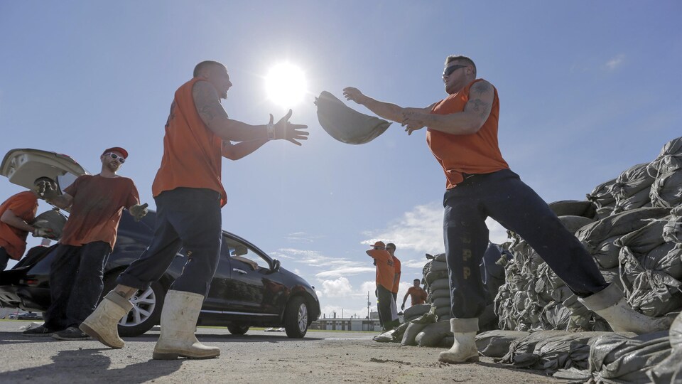 Des hommes chargent des sac de sable dans des voitures,