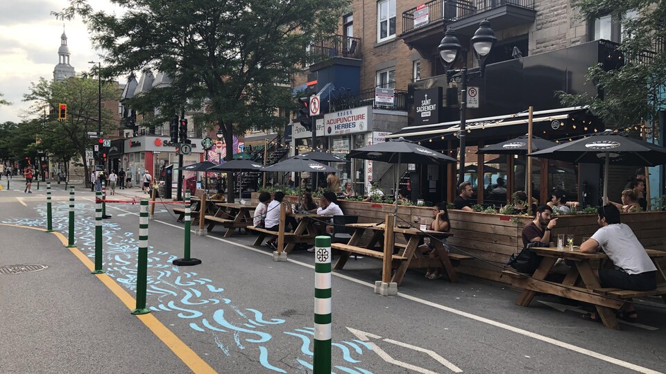 Des clients assis sur des bancs extérieurs devant des bars sur la rue Saint-Denis à Montréal.
