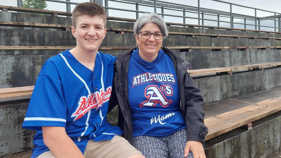 Un adolescent assis avec sa mère dans des estrades de baseball.