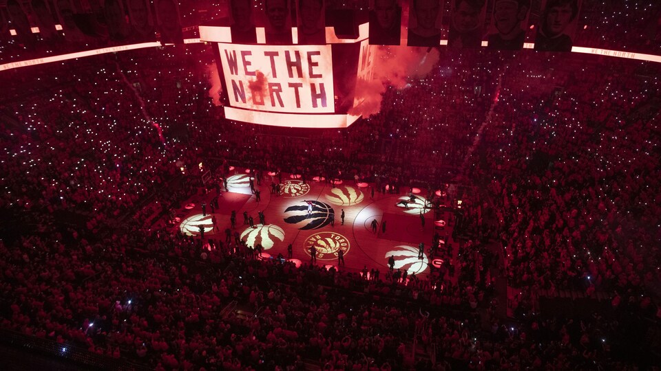 Dans l'aréna plongée dans l'obscurité et des lumières rouges, l'écran géant au centre et au dessus du terrain affiche le slogan We the North.
