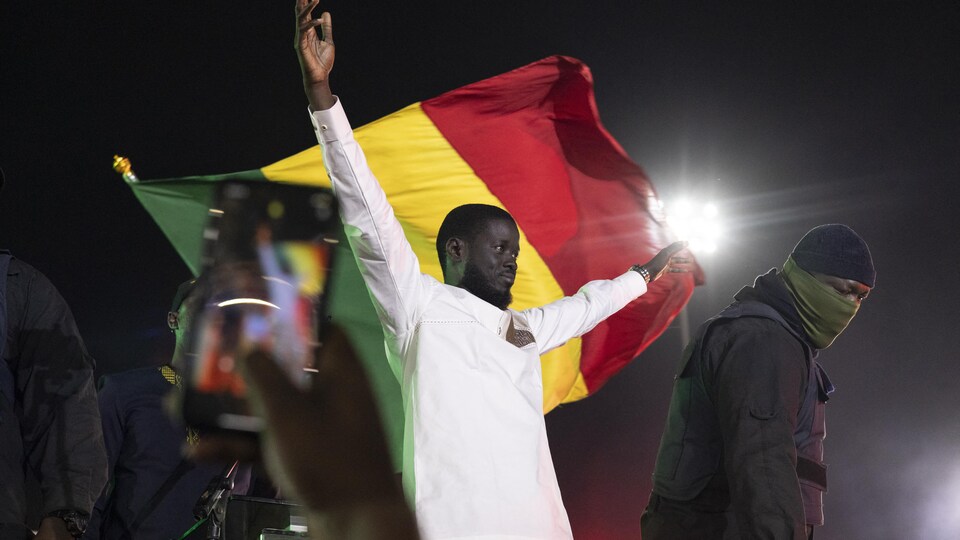 Bassirou Diomaye Faye lève les bras devant un drapeau du Sénégal.