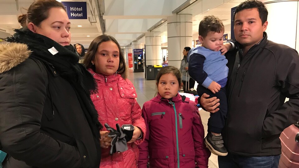 La famille, composée des parents et de trois enfants, le regard triste, attend de prendre l'avion à l'aéroport.