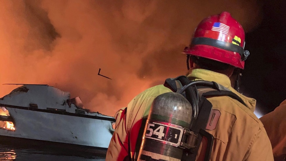 Un pompier est vu de dos, devant le bateau en flammes.
