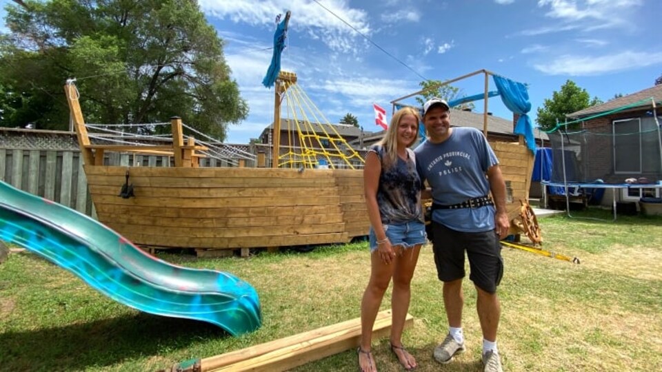 Le couple Konstantinidis se tient debout dans la cour arrière près du bateau en bois.