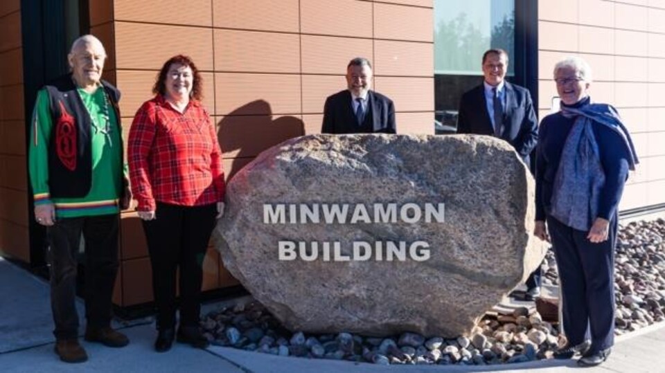 Cinq personnes autour d'une grosse roche où il est inscrit « Minwamon Building ».