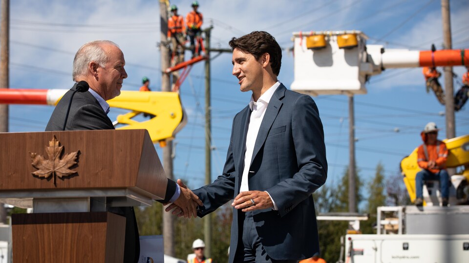 Justin Trudeau et John Horgan échangent une poignée de main devant des employés de BC Hydro, en arrière-plan.