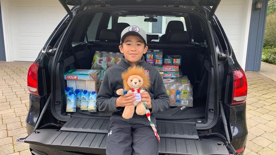 Bear Yeung, un jeune garçon de 9 ans, tient un ourson en peluche devant le coffre arrière d'une voiture pleine de produits alimentaires.