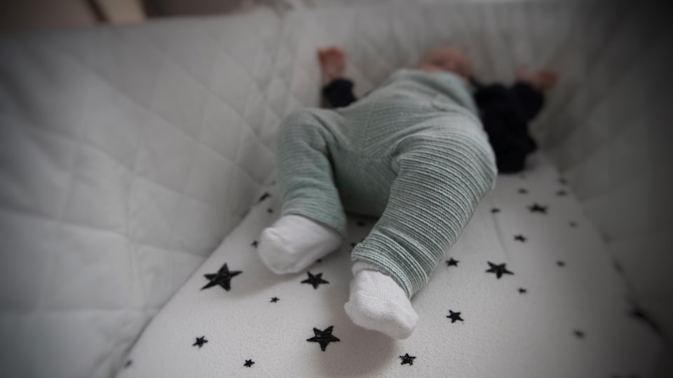 Un bébé couché sur le dos dans son lit, dont on voit les jambes en gros plan.