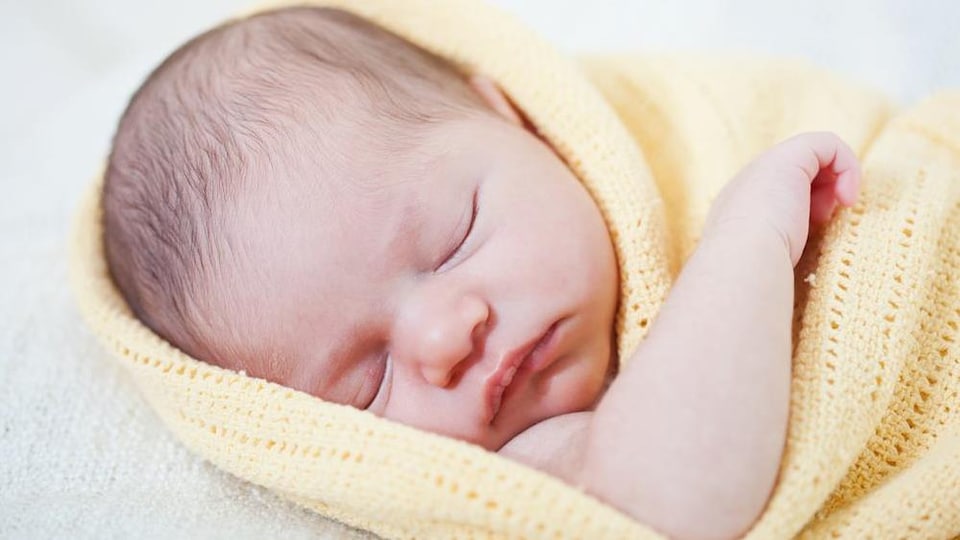 Un bébé nouveau-né dort, enveloppé dans une couverture.