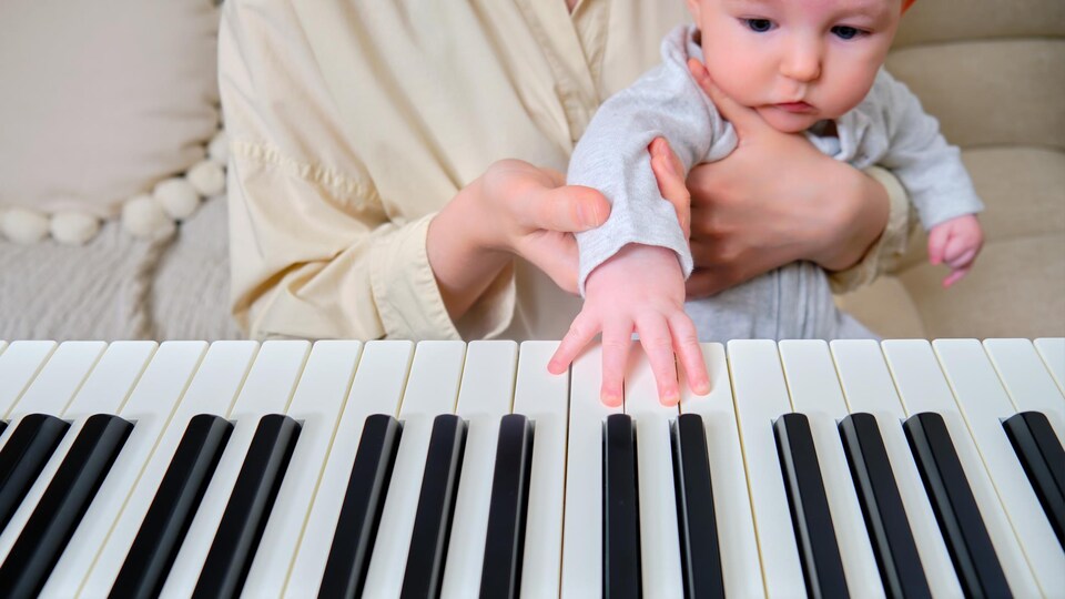 Un bébé pose sa main sur le clavier d'un piano. Il est assis sur les genoux d'une personne.