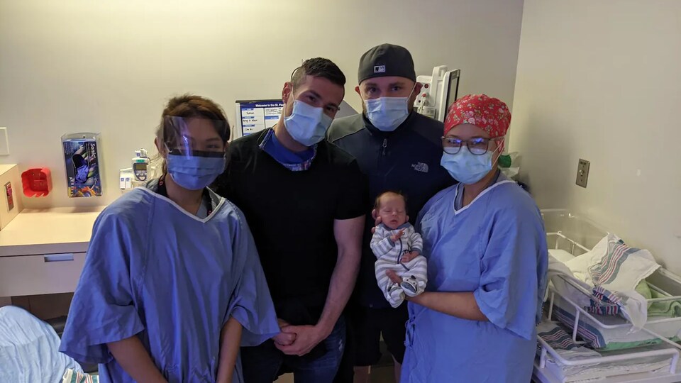 Les infirmières Quyen Tran (à gauche) et Clara Vuong (à droite), font la pose avec les nouveaux parents, Allen Penny (centre gauche) et Greg Shaw (centre droit) ainsi que bébé Yukon.