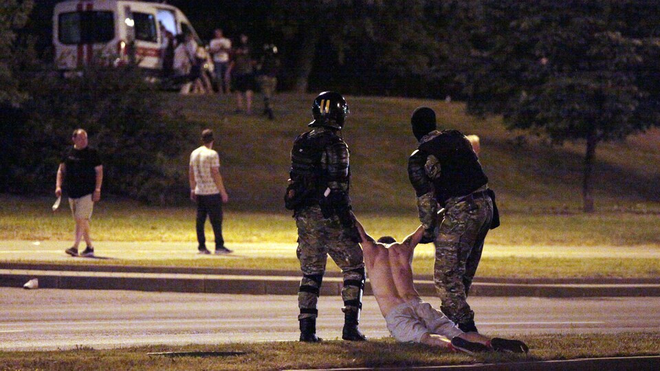 Deux policiers vêtus d'équipement militaire traînent par les bras un manifestant, torse nu.