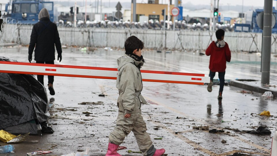 Des enfants marchent devant des colonnes de policiers polonais barricadés derrière des barbelés.