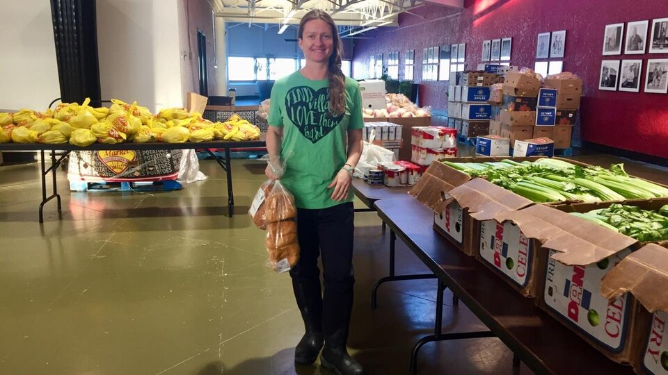 Une femme en T-shirt vert pose au milieu d'une pièce remplie de nourriture.